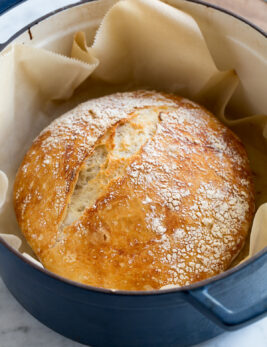No knead bread in a large blue pot resting on parchment paper.