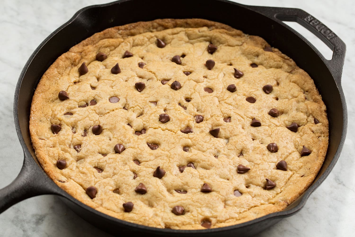 Whole skillet chocolate chip cookie shown in cast iron pan after baking and puffed.