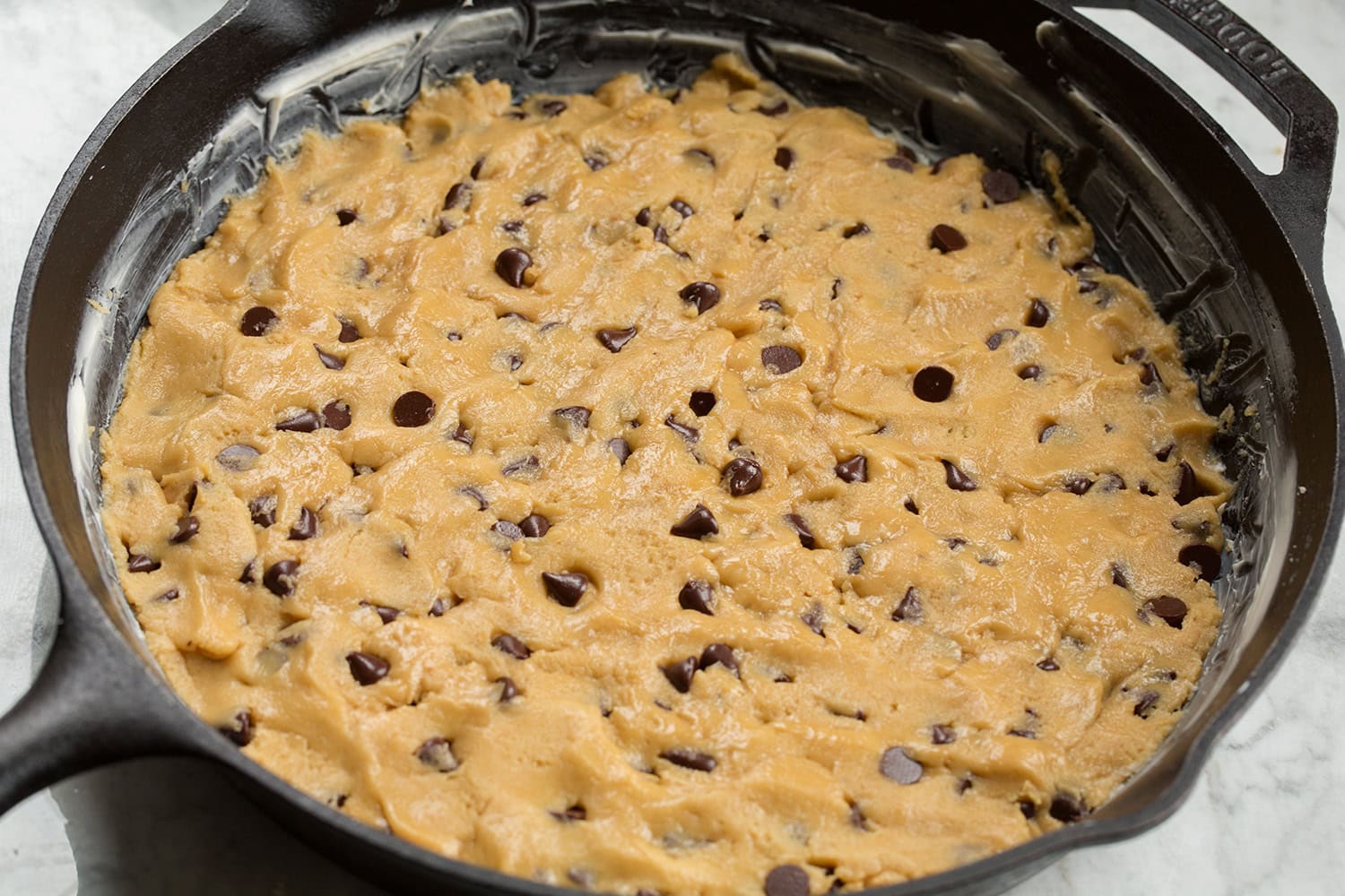 Chocolate chip cookie batter in a cast iron skillet shown before baking.
