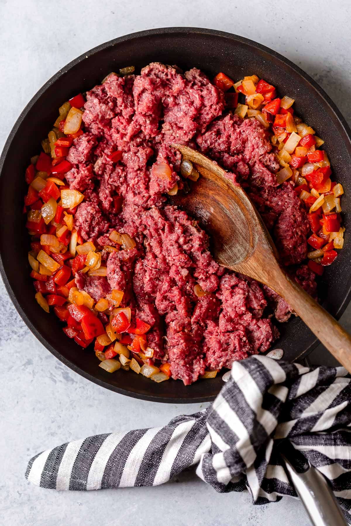 Browning ground beef in a skillet with bell peppers and onions.