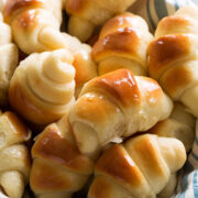 Homemade dinner rolls shown in a basket with a blue striped cloth.