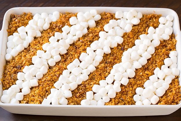 Adding mini marshmallows to sweet potato casserole in rows.
