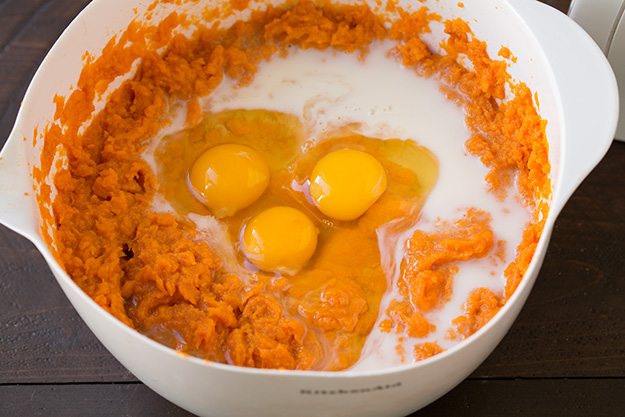 Adding eggs and milk to sweet potatoes in mixing bowl.