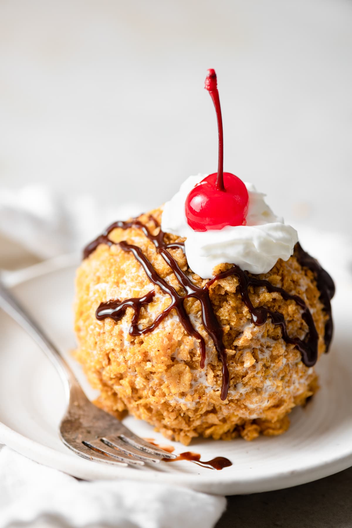 Close up image of fried ice cream on a dessert plate with fork on the left side.