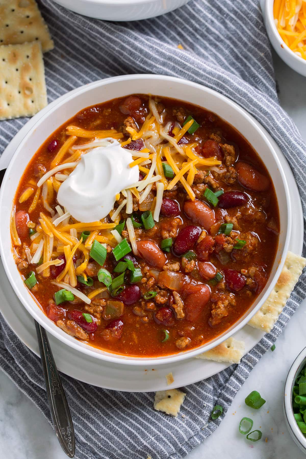 Overhead image of bowl of chili topped with cheddar, sour cream and green onions.