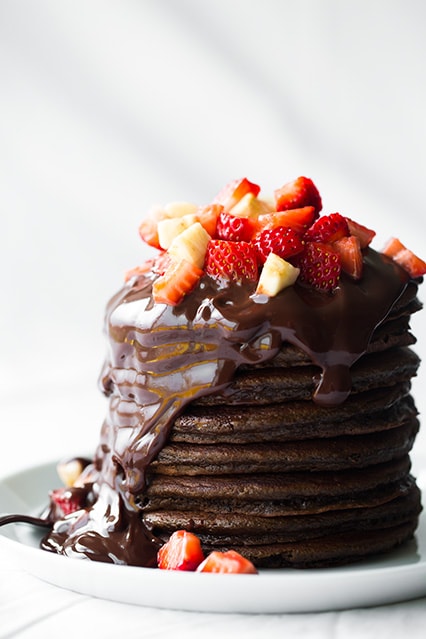 stack of Chocolate Pancakes topped with chocolate sauce and diced fresh fruit on white plate
