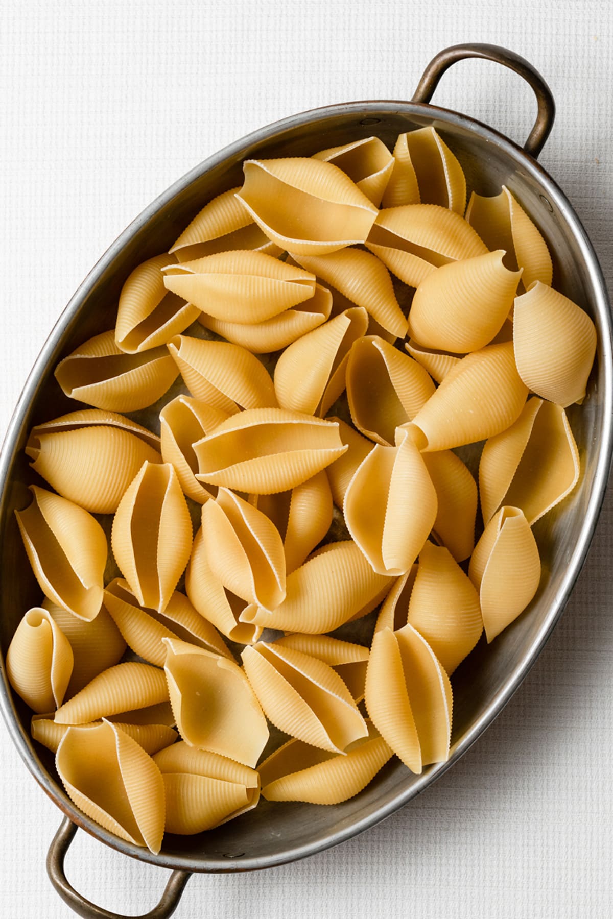 Image of large pasta shells in a oval pewter baking dish.