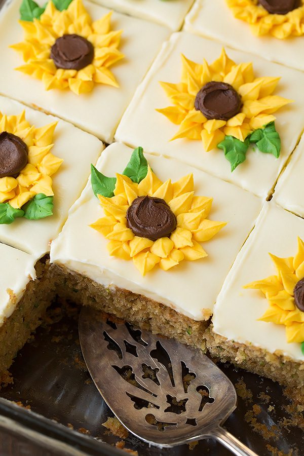 Zucchini Cake with Cream Cheese Frosting in a baking dish cut into slices. Each slice is decorated with a yellow piped buttercream sunflower.