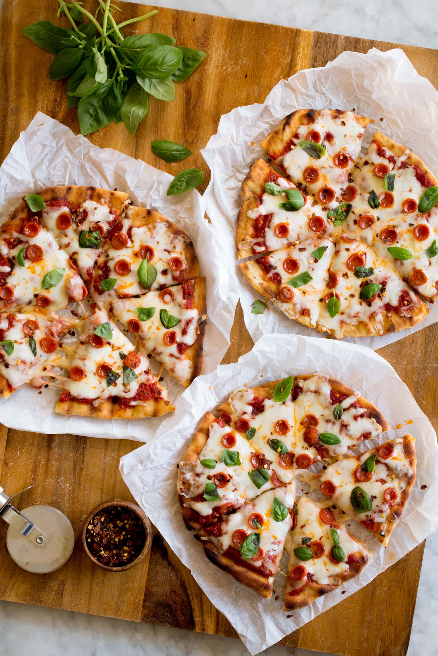 Grilled individual pizzas topped with mozzarella, pepperoni and basil.