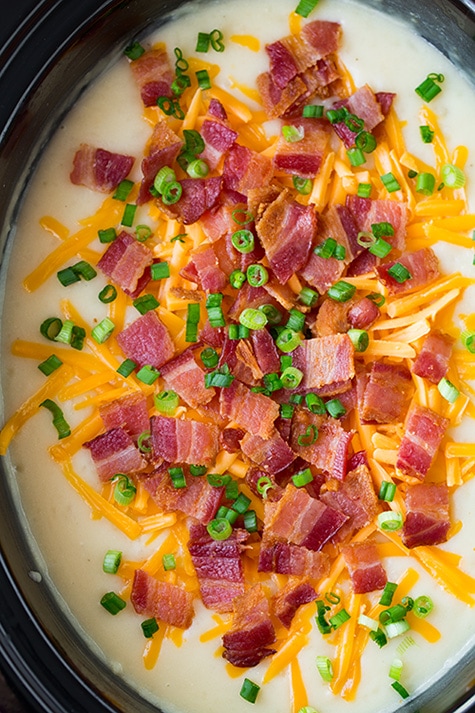 Crockpot potato soup in a slow cooker topped with cheddar, bacon and green onions.