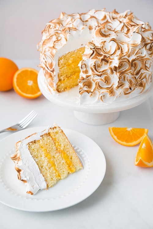 Orange Chiffon Cake with Orange Filling and Meringue on cake stand next to slice of cake on a plate