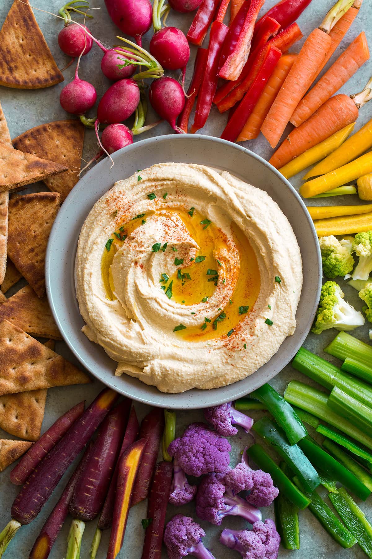 Hummus in a serving bowl surrounded by chips and veggies