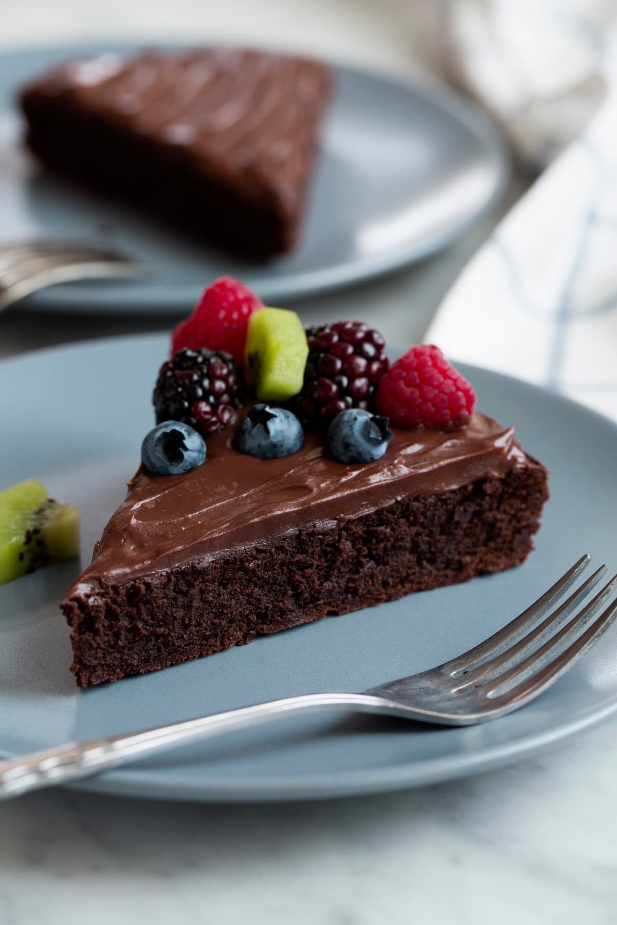 Flourless Chocolate Cake on a blue serving plate. Cake is topped with ganache and fresh fruit.