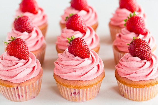 Three rows of strawberry cupcakes topped with strawberry buttercream and fresh strawberries