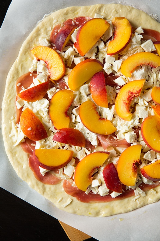 uncooked pizza crust topped with prosciutto and ricotta and fresh peach slices