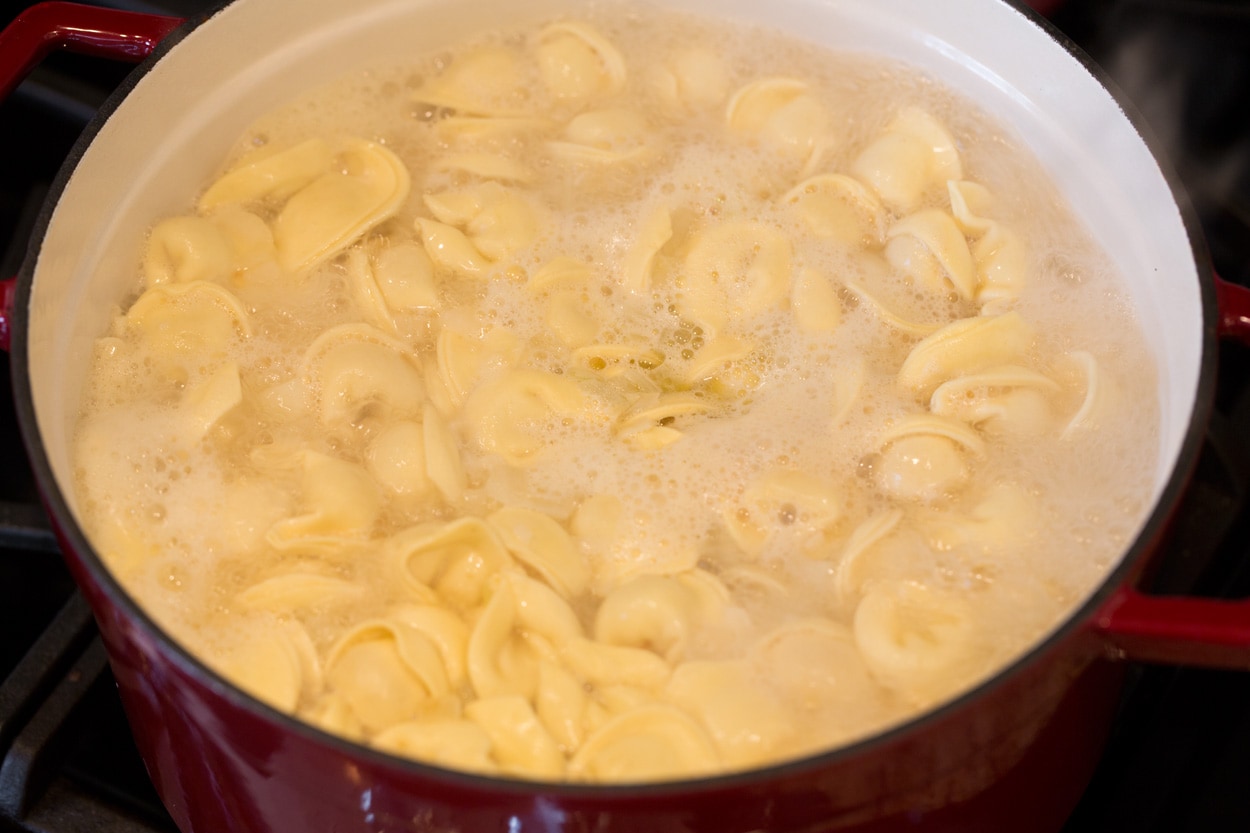Boiling tortellini in broth mixture to make tortellini soup.