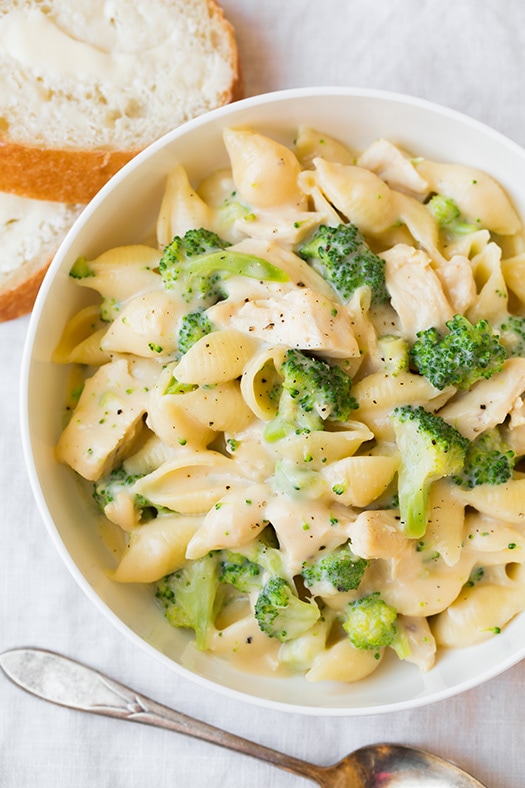 chicken and broccoli pasta in white bowl next to bread slices