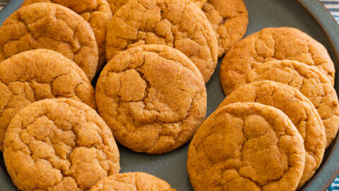 Pumpkin snickerdoodle cookies on a blue plate with white pumpkins and cinnamon sticks around it for decoration.