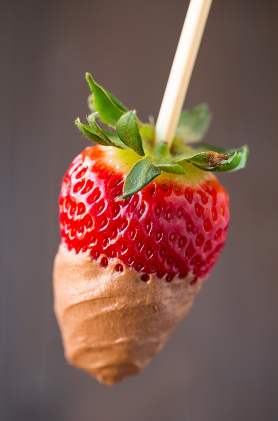Close up image of chocolate fruit dip covering a fresh strawberry on a skewer