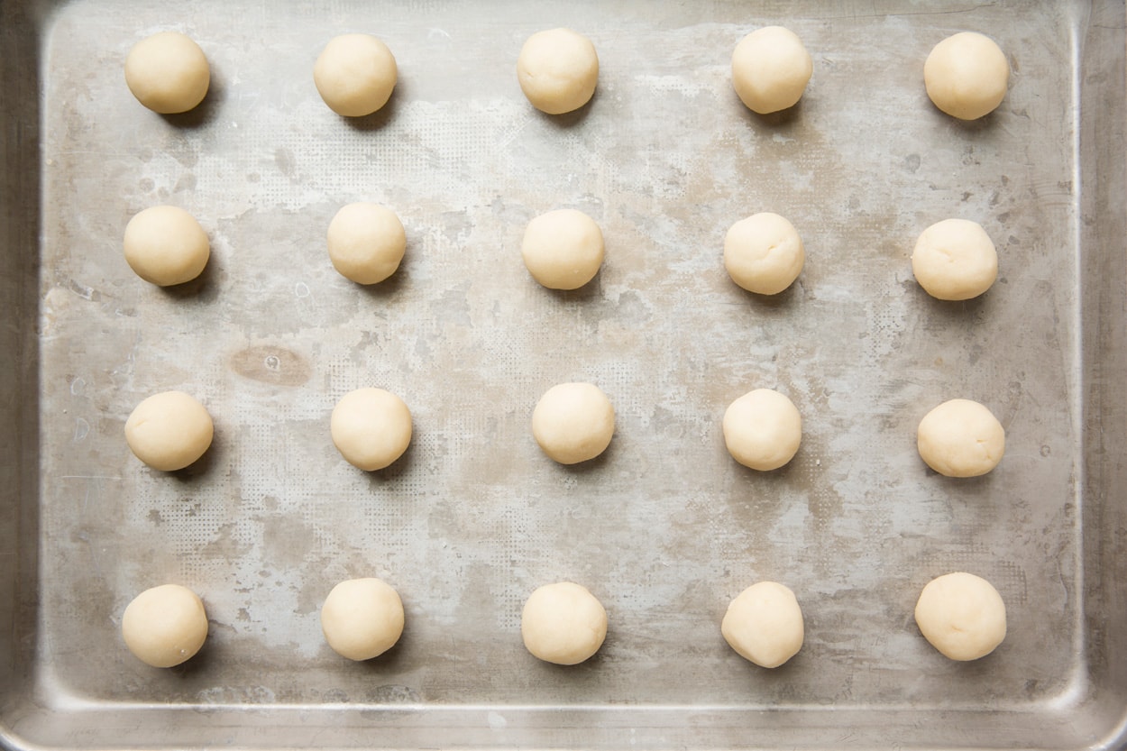Showing how to make thumbprint cookies. Shortbread cookie dough rolled into rounds and placed on un-greased baking sheet.