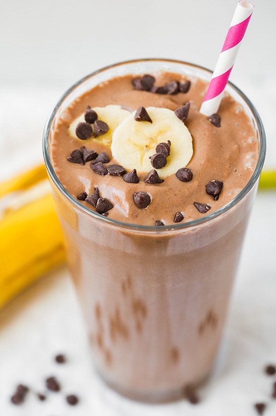 A chocolate banana shake in a tall glass topped with chocolate chips