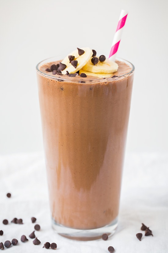 A chocolate banana shake in a glass topped with slices of banana and chocolate chips