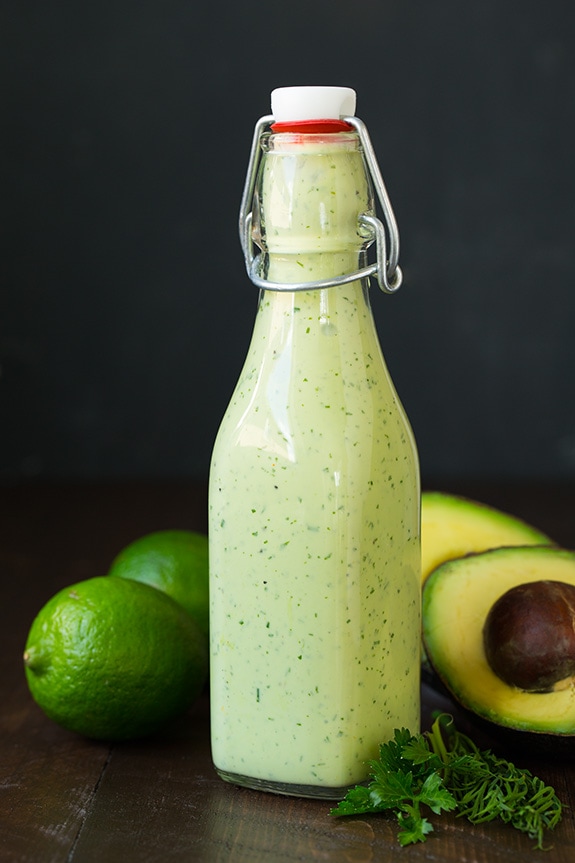 avocado ranch dressing in glass bottle next to fresh limes, cilantro and avocado