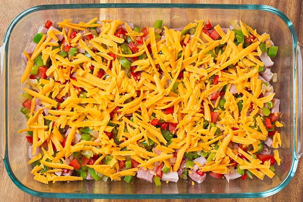 shredded cheddar atop ham and diced veggies in glass baking dish