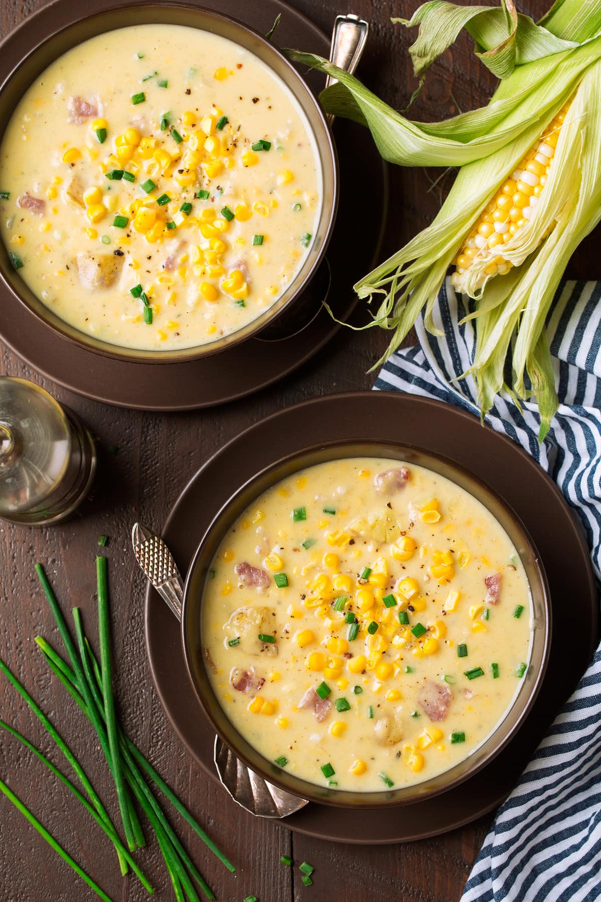 Two serving of corn chowder in brown serving bowls set on plates.