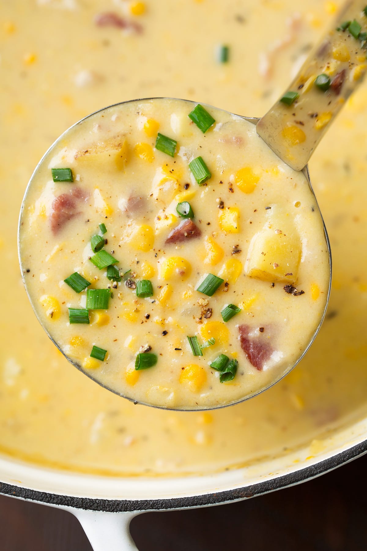Close up image of corn chowder with potatoes in a ladle.