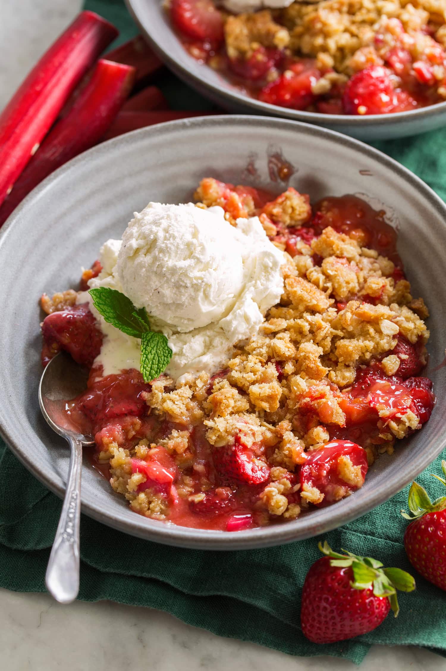 Single serving of strawberry rhubarb crisp shown in a grey bowl with ice cream on top.