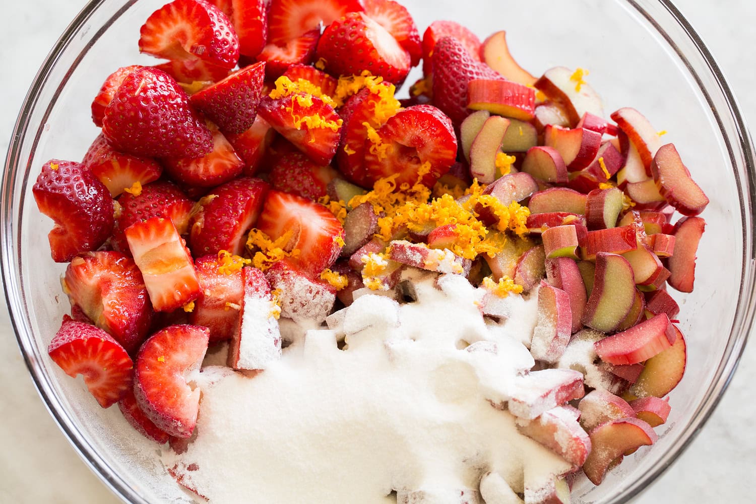 Strawberries, rhubarb and sugar in a glass mixing bowl.