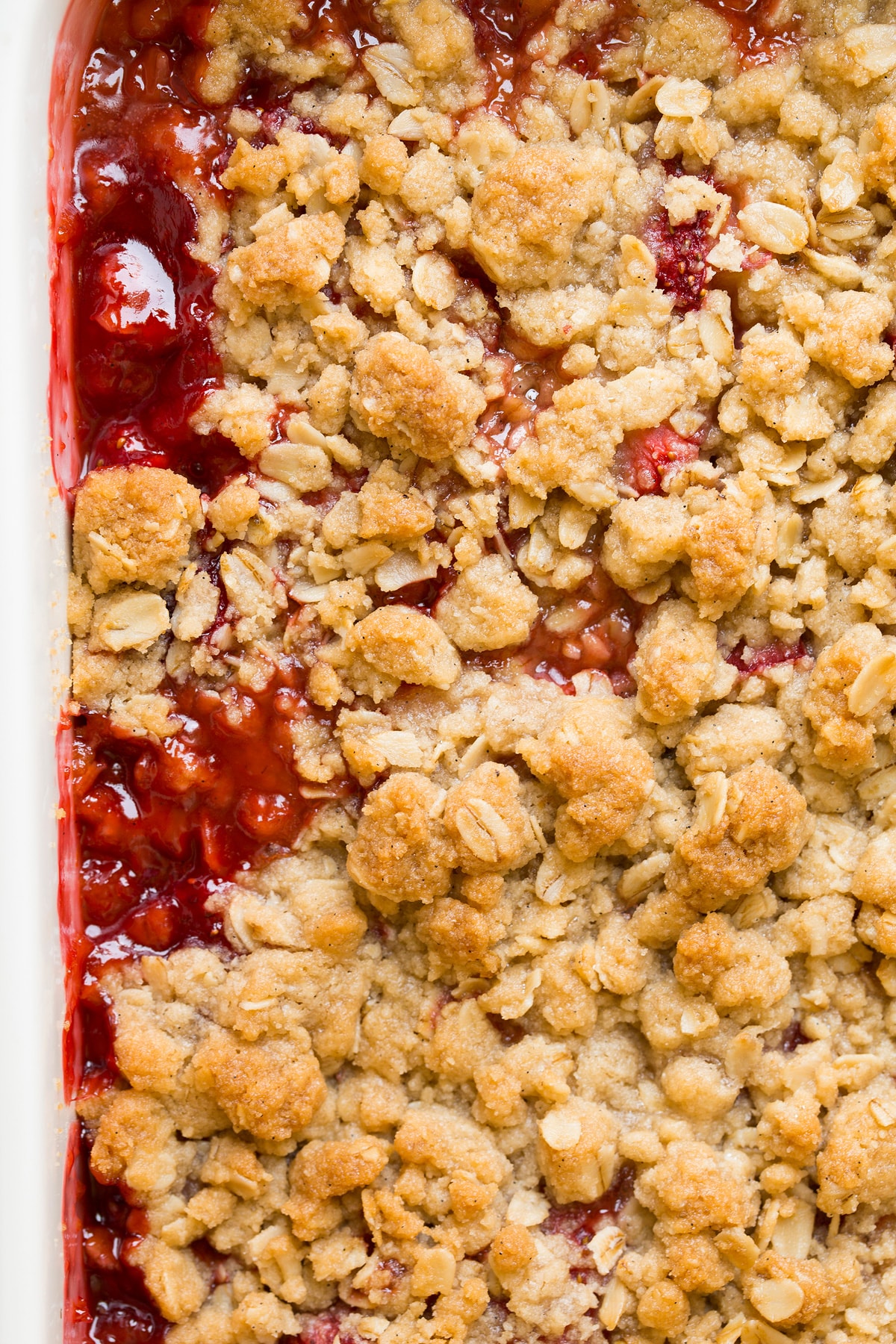 Close up image of baked strawberry rhubarb crisp in a white ceramic baking dish.