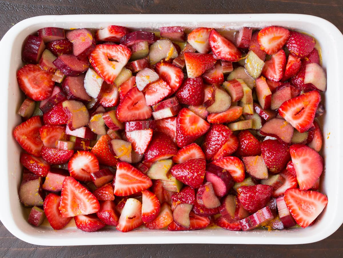 Showing steps to layering strawberry rhubarb crisp. Adding fresh strawberries and rhubarb to baking dish.