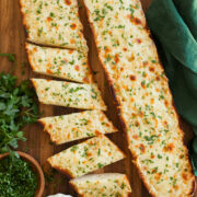 Two halves of cheese garlic bread on a cutting board, one is cut into slices.