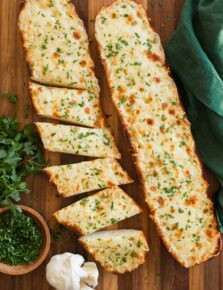Two halves of cheese garlic bread on a cutting board, one is cut into slices.
