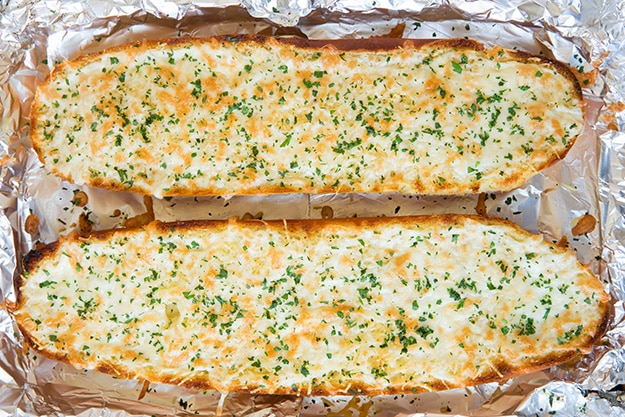 two halves of a loaf of cheesy garlic bread on foil