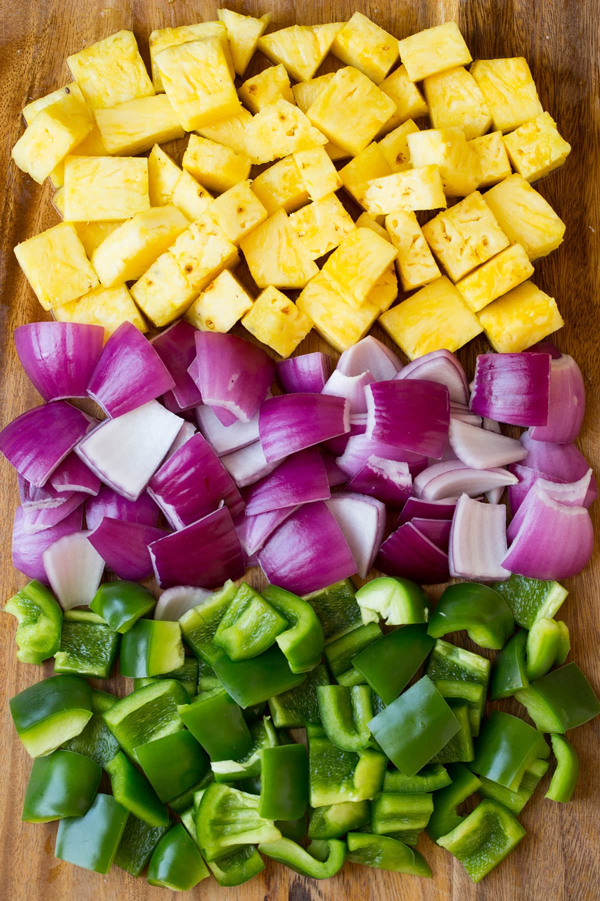 Pineapple red onion and bell pepper pieces on a wooden cutting board.