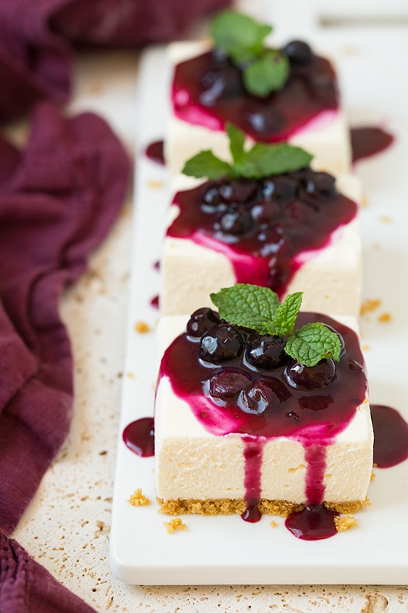 Three no bake cheesecake servings on a platter, topped with blueberry sauce and mint.