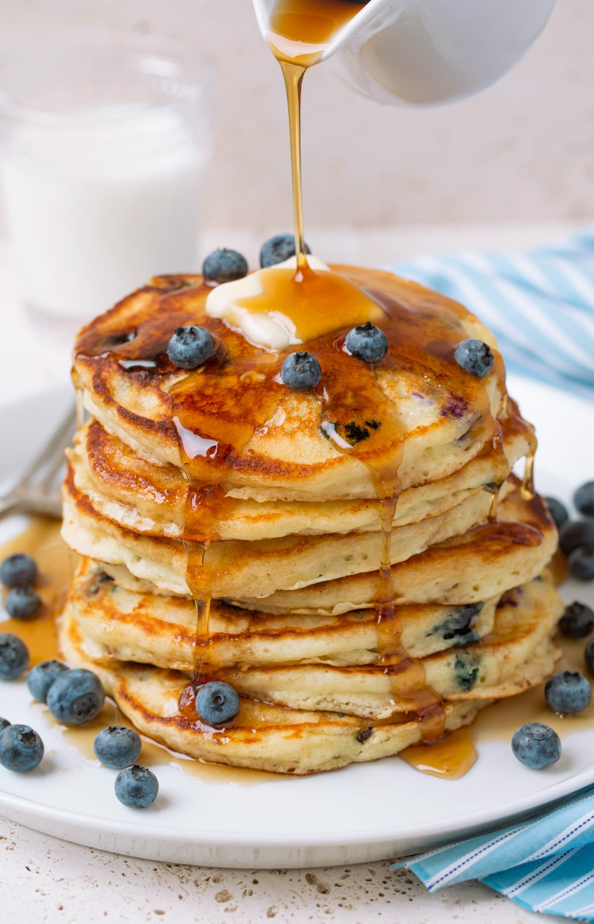 Pouring syrup over stack of homemade blueberry pancakes