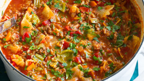 Cabbage Roll Soup shown in a large white pot on a blue cloth.