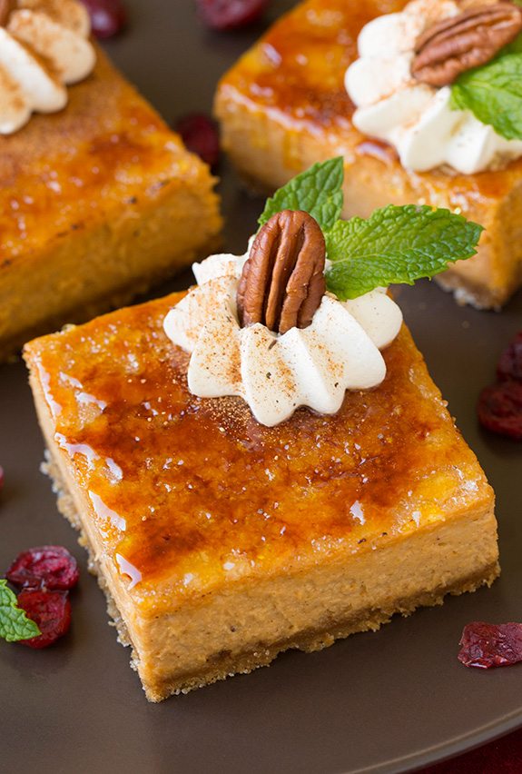 Pumpkin cheesecake bars topped with a toasted sugar brulee topping, whipped cream, pecans and mint leaves.