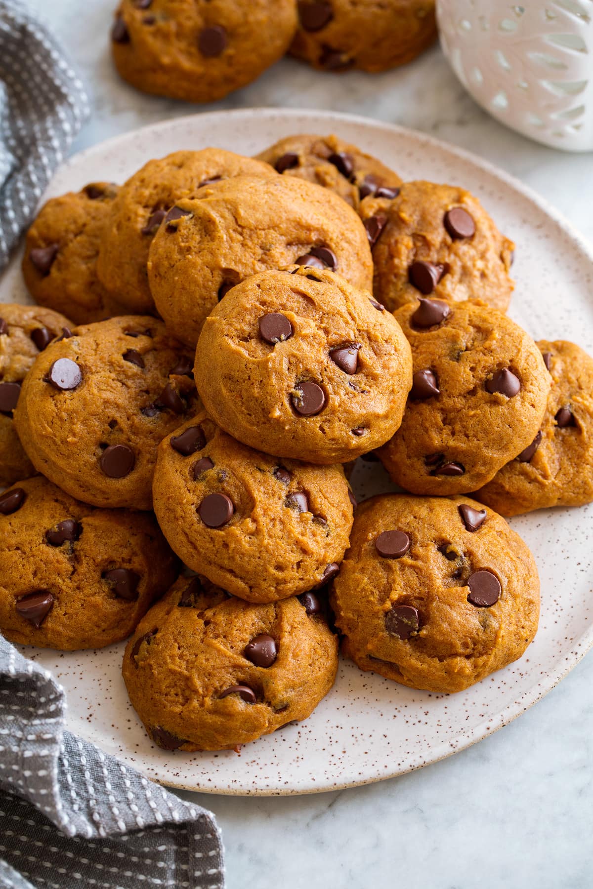 Image of pumpkin chocolate chip cookies stacked on a white serving plate.