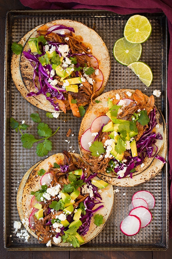 three slow cooker pork tacos on baking tray with sliced radishes and lime wedges