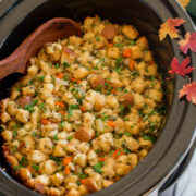 Stuffing in a crockpot with decorative fall leaves and a green cloth to the side.