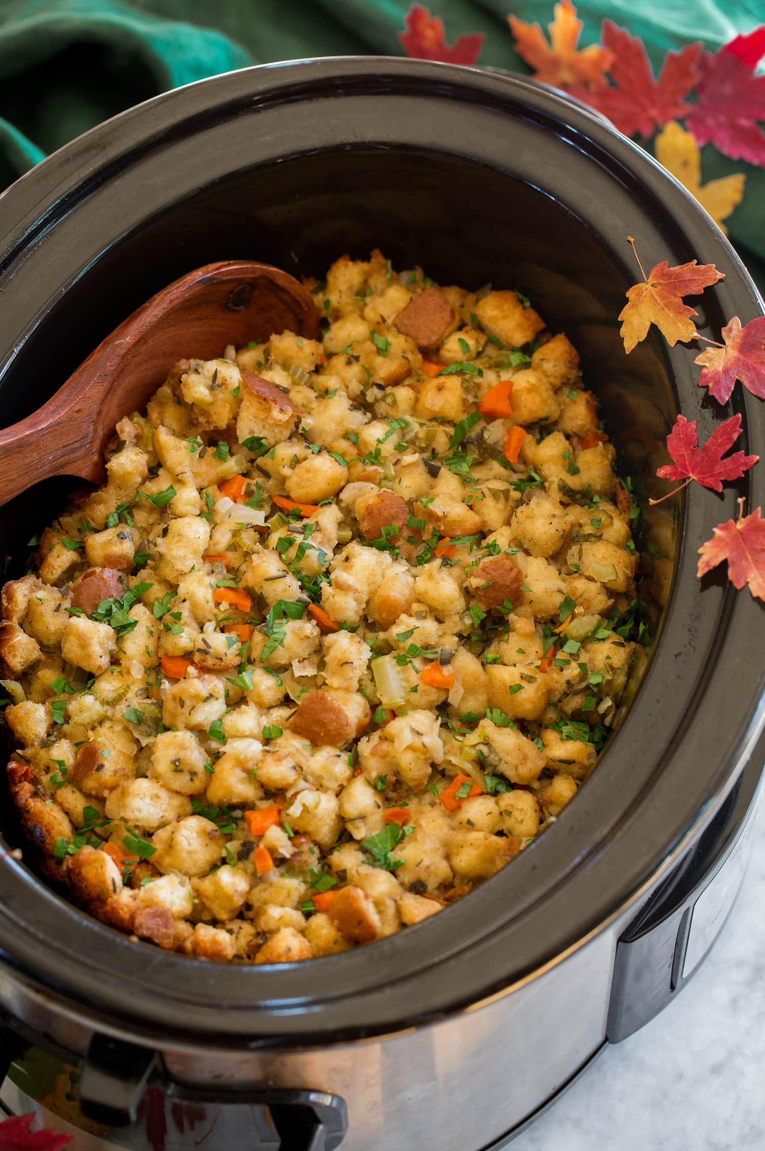 Fill in a slow cooker with decorative autumn leaves and a green cloth on the side.