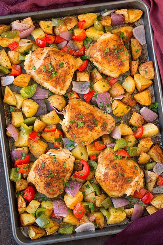 Overhead image of baked cajun chicken thighs and veggies on a sheet pan.