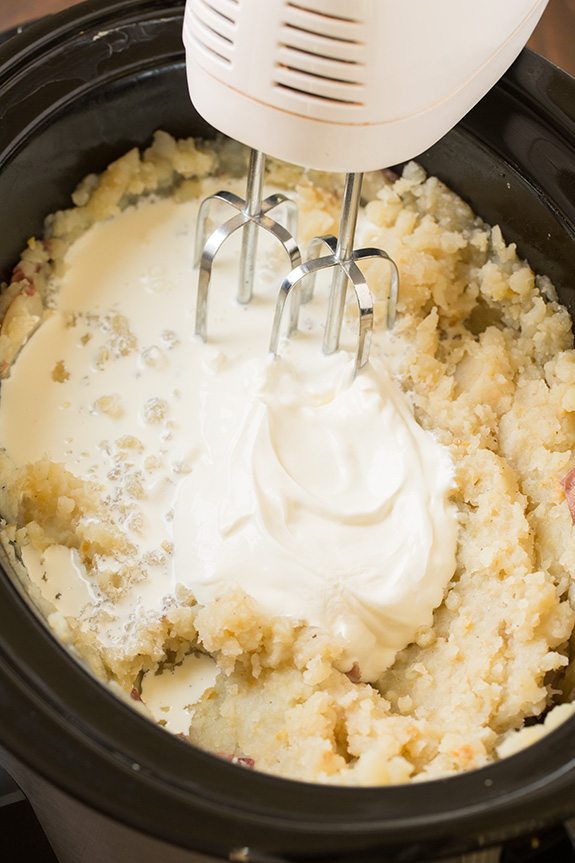 Mixing milk and sour cream in to mashed potatoes with an electric hand mixer.