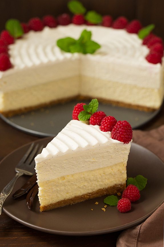 Slice of cheesecake on a plate with a whole cheesecake in the background.