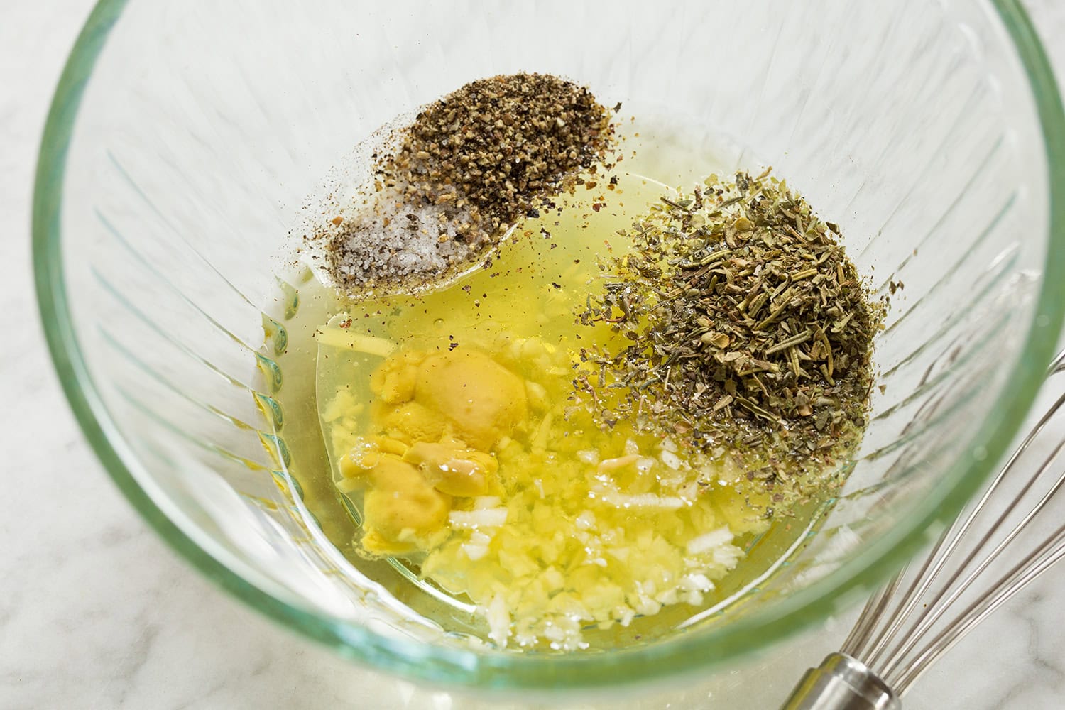 Caprese Chopped Salad Chicken marinade shown in a glass bowl before mixing. Includes oil, lemon, dijon, herbs and garlic.